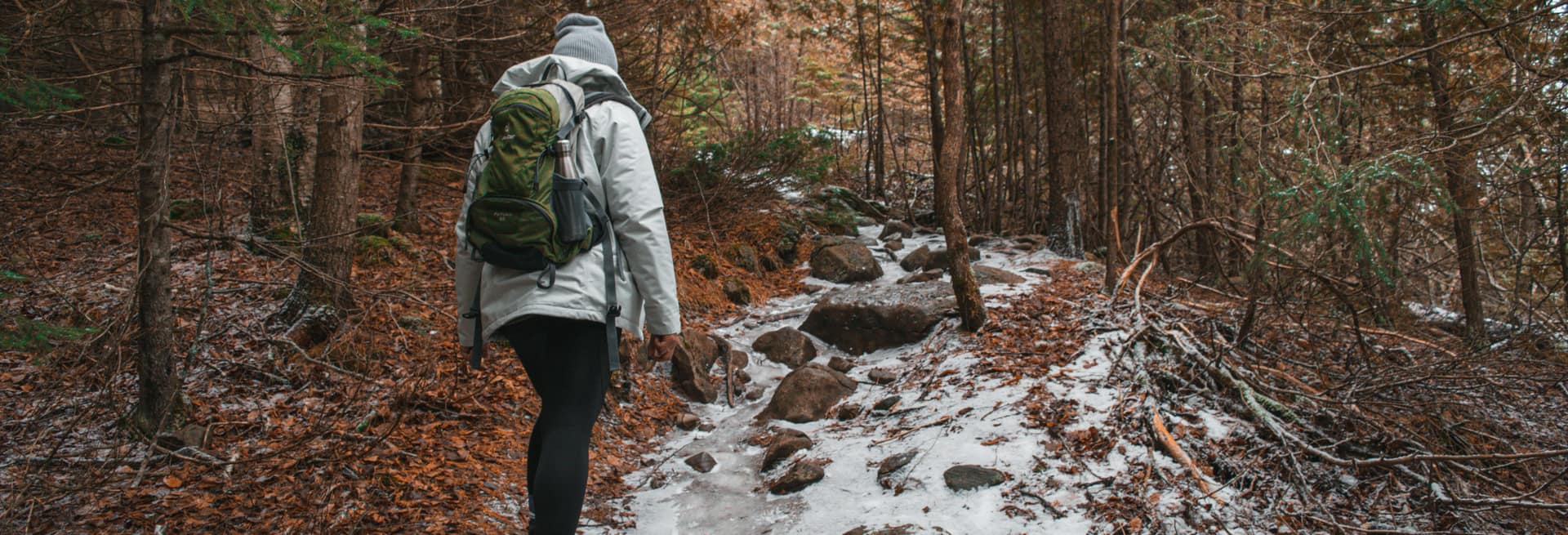 Person mit Rucksack auf einem verschneiten Waldweg
